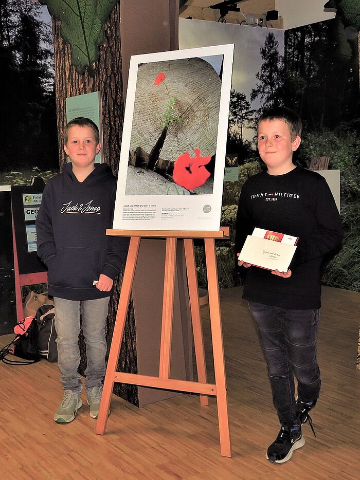 Die zwei 9jährigen Brüder Jakob und Anton stolz vor ihrem Gewinnerfoto mit dem sie den Sonderpreis in der Kategorie "Verändern, vergehen, verwandeln" gewonnen haben. Sie freuen sich auch über den Gutschein des Naturium am Inn für eine Führung ins Europareservat Unterer Inn. (Foto: Naturium)